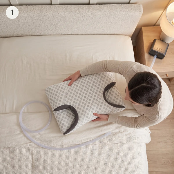 Hands aligning the pillow's side cutout with a CPAP hose on the bed